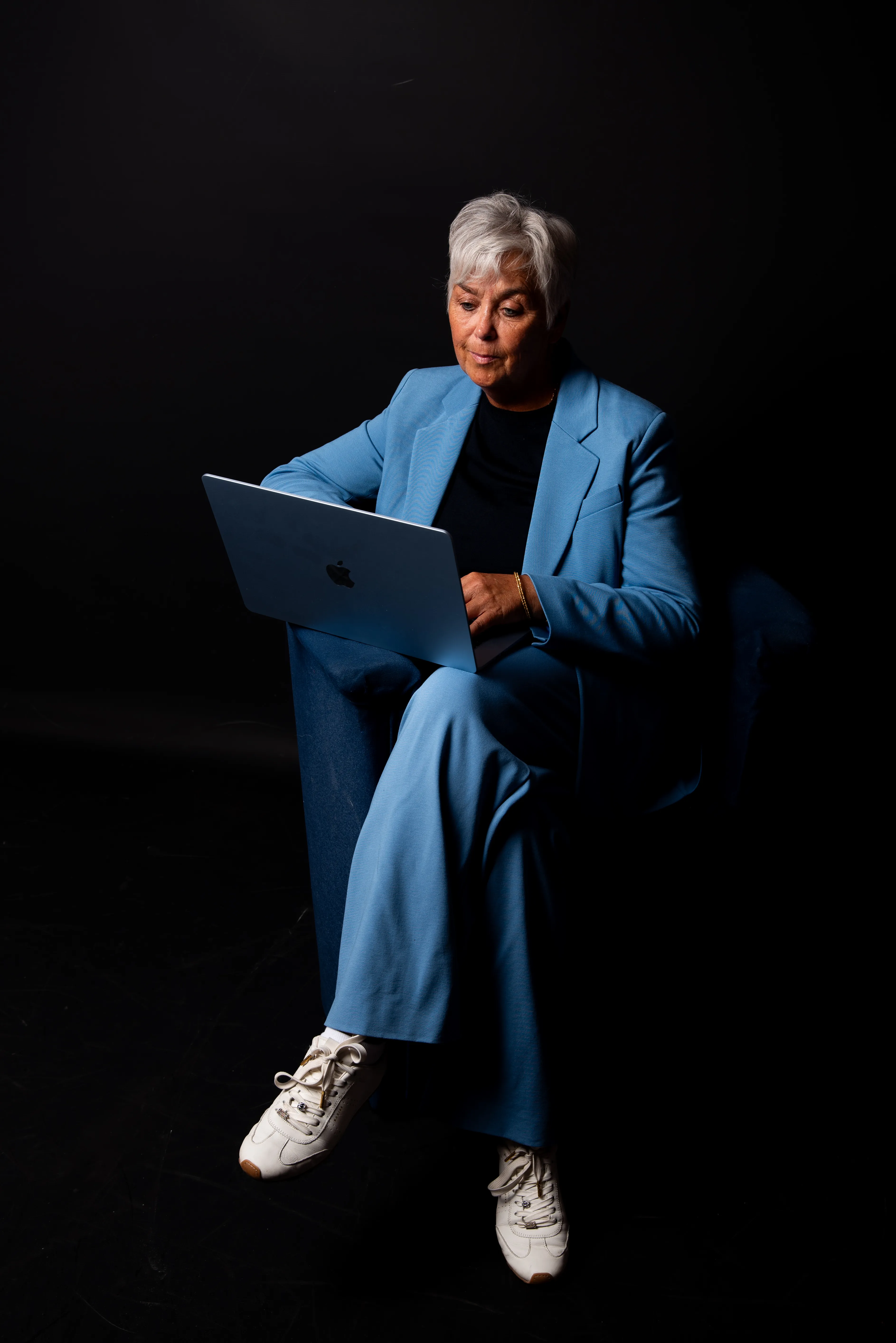 Arlette Vonk, blue suit, black backdrop, working at her laptop