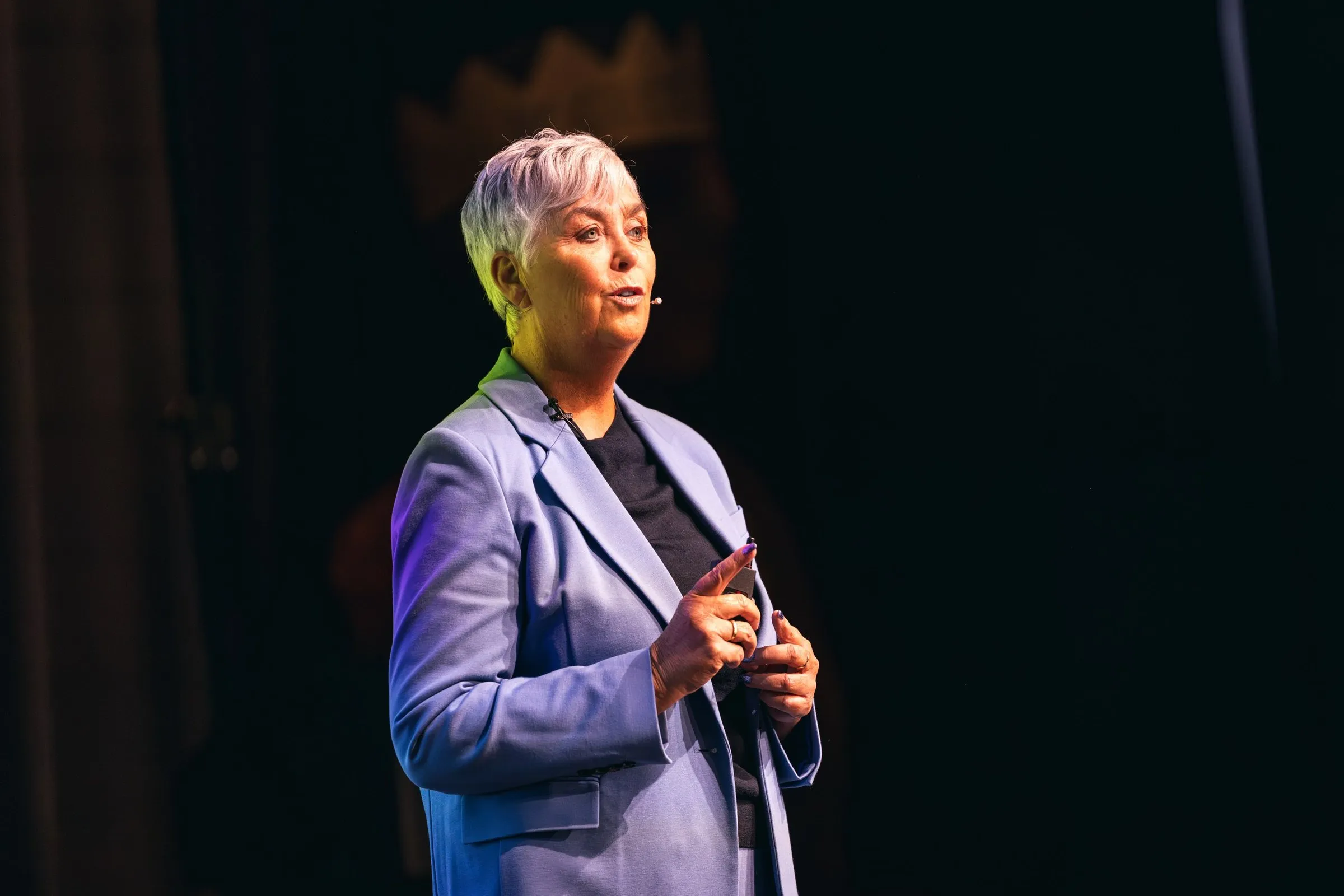 Arlette Vonk speaking on a darkened stage, clicker in hand, mid sentence